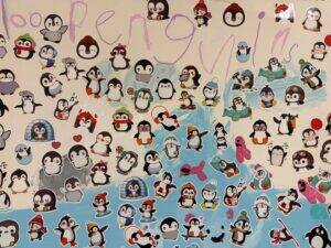 A collage of colorful penguin stickers covers a surface, with some penguins wearing hats and scarves. Above them, 100 penguins is written in large, pink handwriting. The background is white and blue.